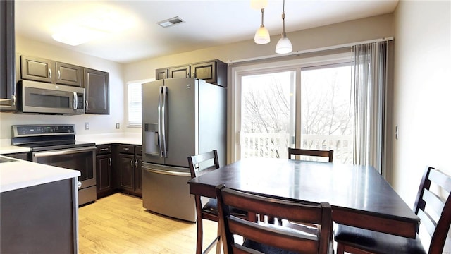 kitchen with appliances with stainless steel finishes, dark brown cabinets, hanging light fixtures, and light hardwood / wood-style floors