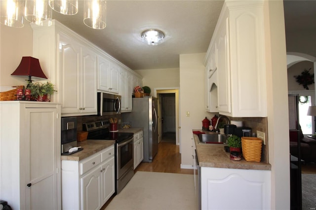 kitchen featuring decorative light fixtures, tasteful backsplash, sink, white cabinets, and stainless steel appliances