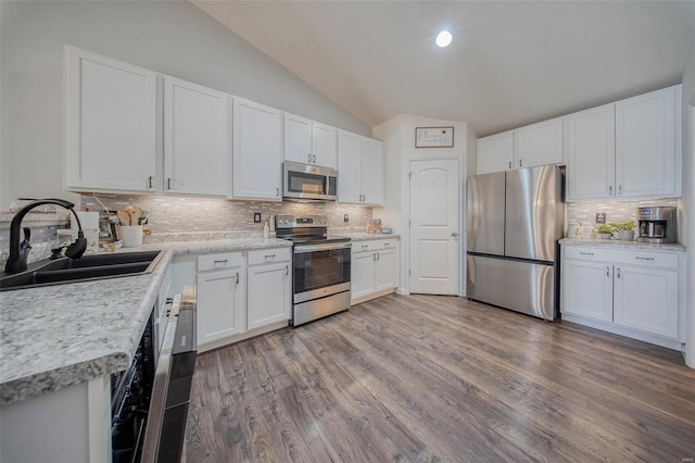 kitchen with vaulted ceiling, sink, white cabinets, backsplash, and stainless steel appliances