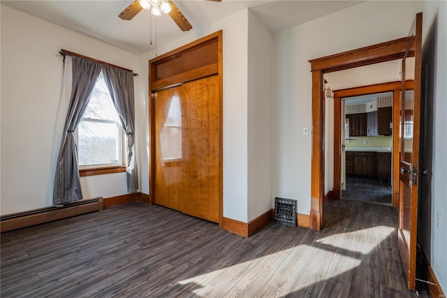 unfurnished bedroom featuring dark wood-type flooring, ceiling fan, and a baseboard heating unit