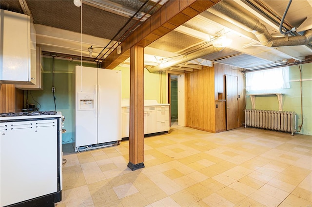 basement with wooden walls, radiator, and white fridge with ice dispenser