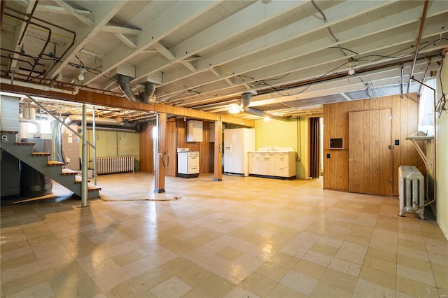 basement with white refrigerator with ice dispenser, radiator, wooden walls, and washer / clothes dryer