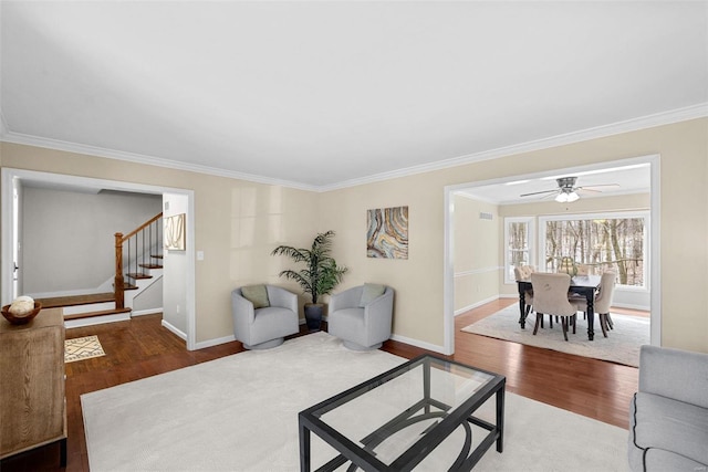 living area with baseboards, crown molding, stairway, and wood finished floors