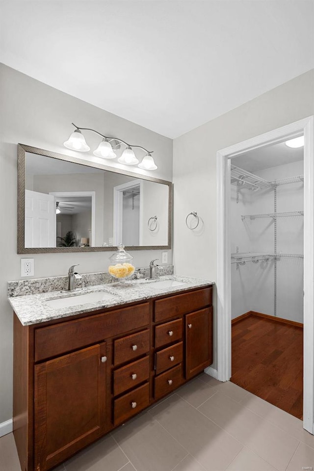 full bathroom with double vanity, baseboards, tile patterned flooring, a walk in closet, and a sink