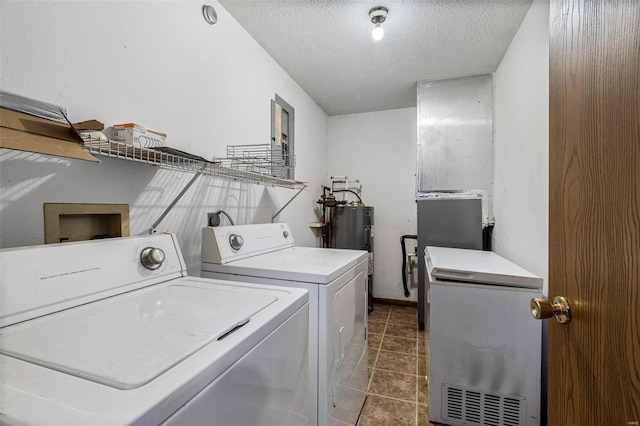 laundry area with dark tile patterned floors, washing machine and dryer, water heater, and a textured ceiling