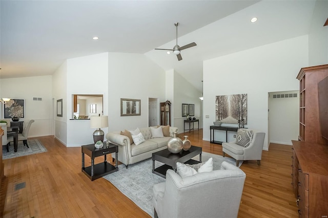 living room featuring ceiling fan with notable chandelier, high vaulted ceiling, and light wood-type flooring