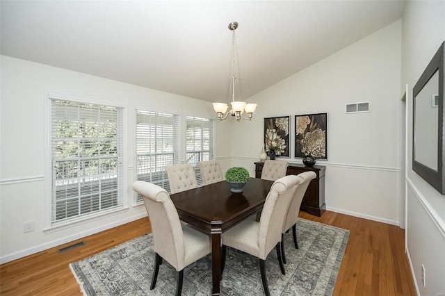 dining space featuring an inviting chandelier, hardwood / wood-style flooring, and vaulted ceiling