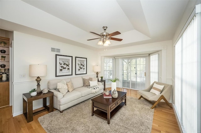 living room with wood-type flooring, ceiling fan, and a tray ceiling