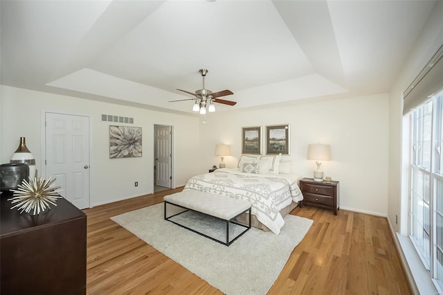 bedroom featuring ceiling fan, a tray ceiling, and light hardwood / wood-style floors