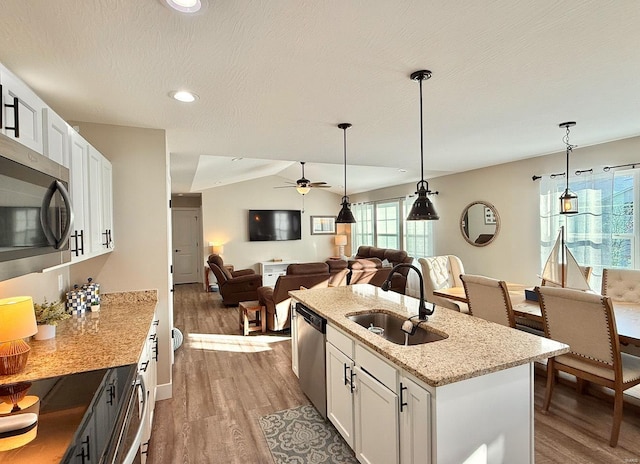 kitchen with white cabinets, open floor plan, light stone countertops, stainless steel appliances, and a sink