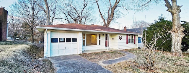 ranch-style house featuring an attached garage, a chimney, and aphalt driveway