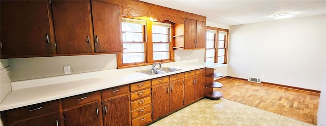 kitchen featuring baseboards, visible vents, light countertops, light floors, and a sink