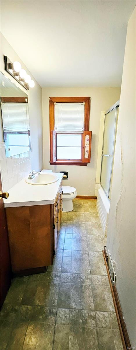 bathroom with baseboards, visible vents, toilet, combined bath / shower with glass door, and vanity