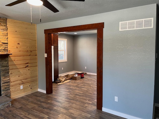 unfurnished living room with ceiling fan, dark hardwood / wood-style floors, a fireplace, a textured ceiling, and wood walls