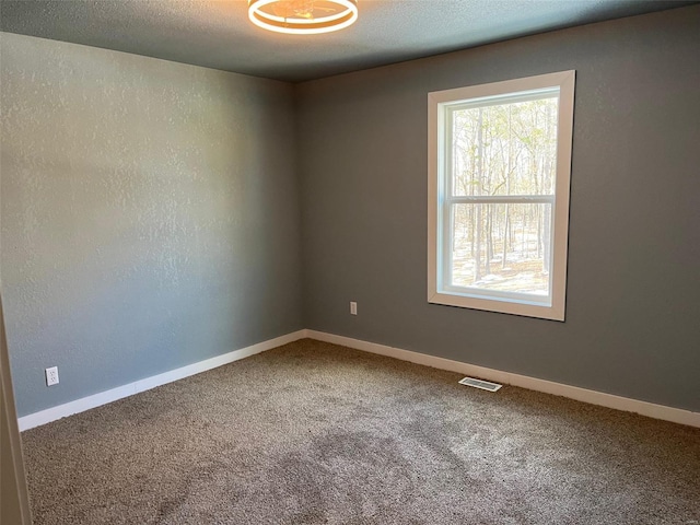 empty room with visible vents, a textured ceiling, carpet, baseboards, and a textured wall