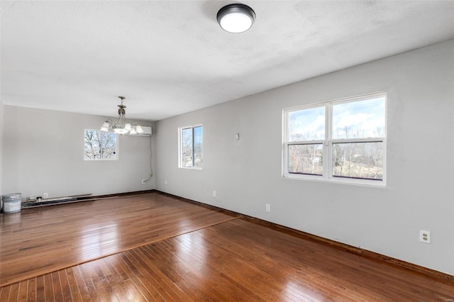 spare room with a notable chandelier, a healthy amount of sunlight, and wood-type flooring