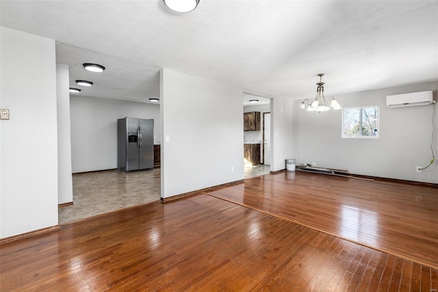 unfurnished living room featuring a wall mounted air conditioner, hardwood / wood-style floors, and an inviting chandelier