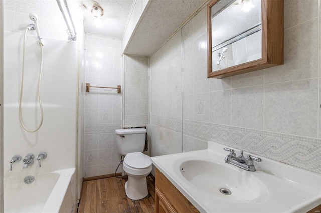 full bathroom with toilet, hardwood / wood-style floors, tile walls, vanity, and  shower combination