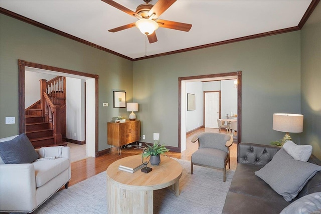 living room with stairway, a ceiling fan, baseboards, light wood-style flooring, and ornamental molding