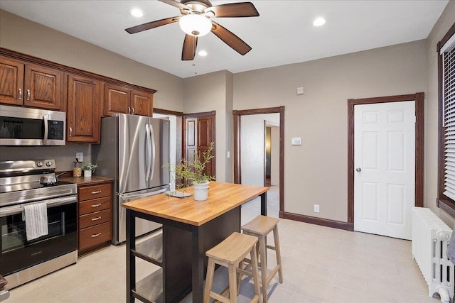 kitchen featuring a breakfast bar area, radiator, wooden counters, recessed lighting, and stainless steel appliances