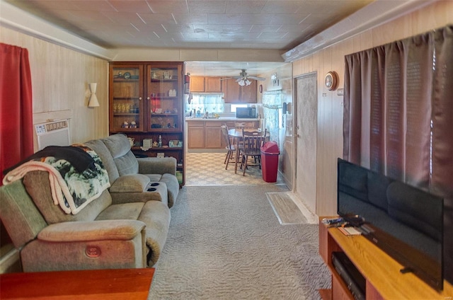 carpeted living room with sink, wood walls, and ceiling fan