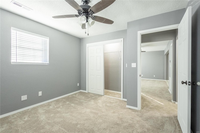 unfurnished bedroom with light carpet, a textured ceiling, ceiling fan, and a closet