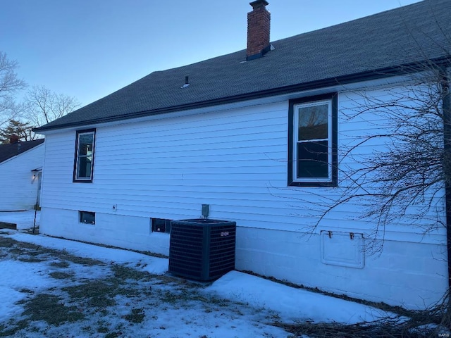 view of snow covered exterior featuring a chimney and central AC unit