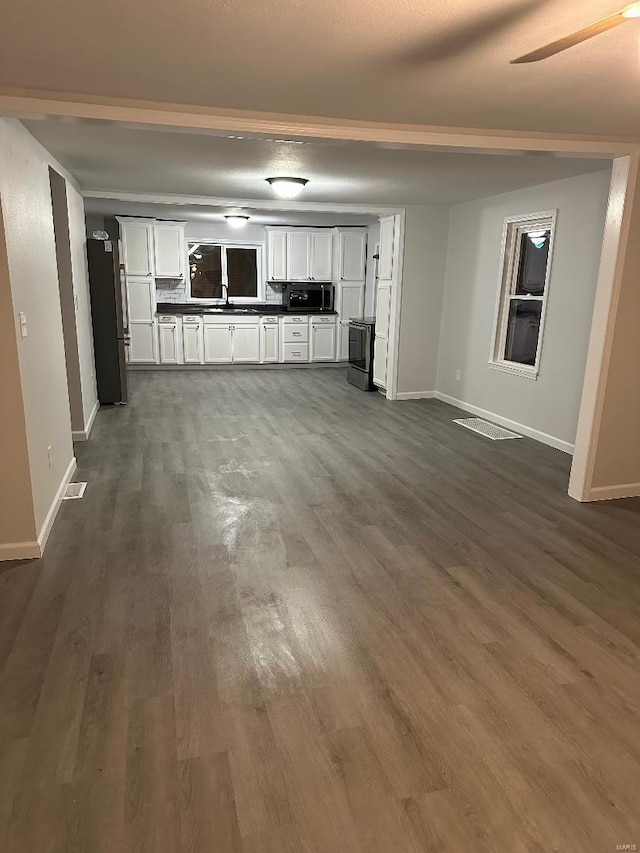 unfurnished living room with visible vents, baseboards, dark wood-style flooring, and a sink