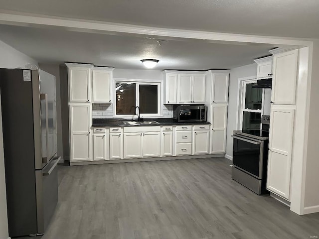 kitchen with range with electric stovetop, decorative backsplash, freestanding refrigerator, white cabinets, and a sink