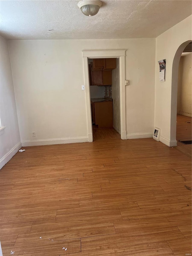 empty room with light wood-type flooring and a textured ceiling