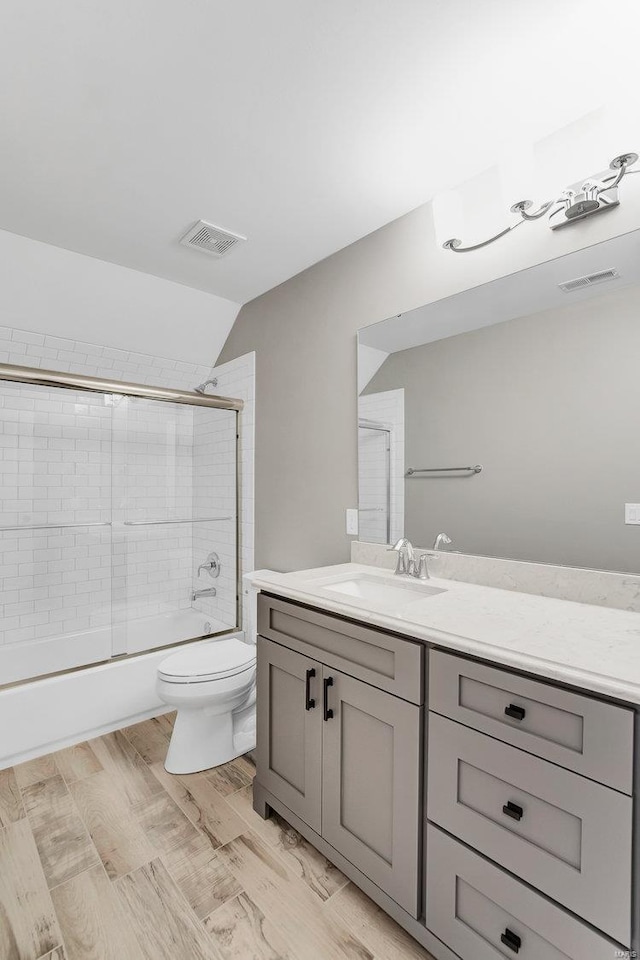 full bathroom with vanity, wood finished floors, visible vents, bath / shower combo with glass door, and toilet