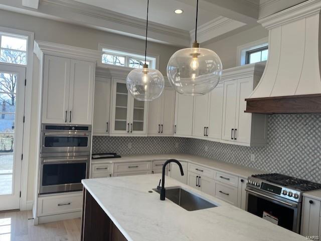 kitchen featuring premium range hood, ornamental molding, a sink, light stone counters, and appliances with stainless steel finishes