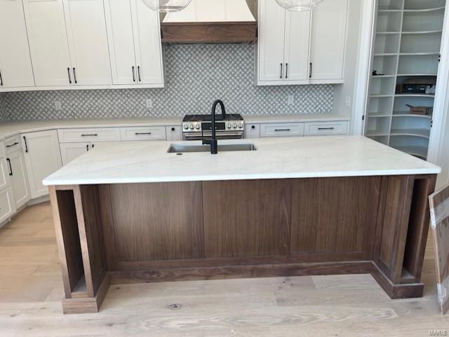 kitchen featuring a kitchen island with sink, under cabinet range hood, a sink, backsplash, and white cabinets