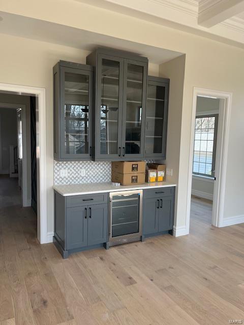 bar featuring wine cooler, tasteful backsplash, crown molding, and light wood finished floors