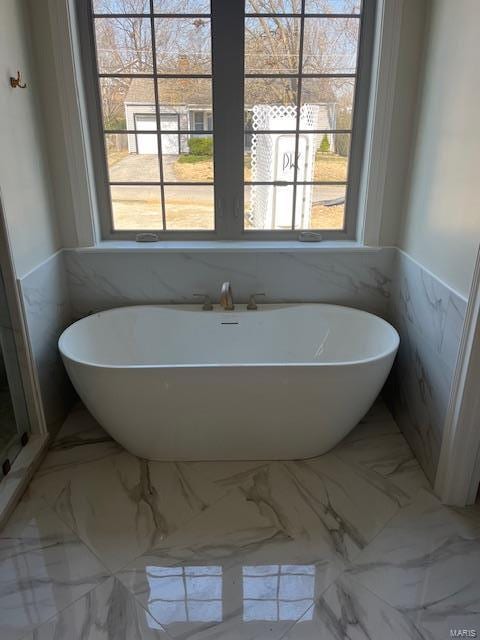 bathroom featuring a freestanding tub, marble finish floor, and a healthy amount of sunlight