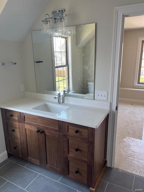 bathroom with vanity, lofted ceiling, baseboards, and tile patterned flooring