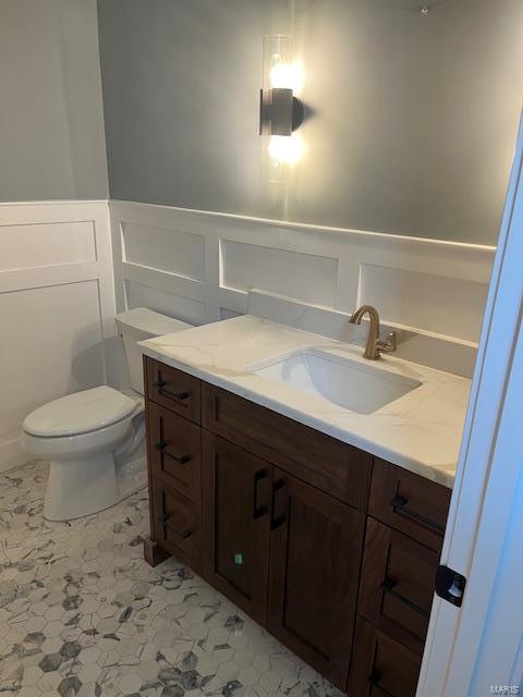 bathroom featuring a wainscoted wall, toilet, and vanity