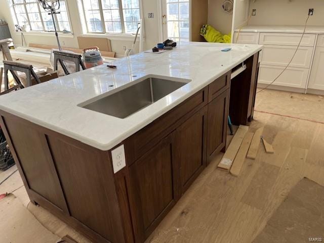 kitchen with a center island with sink, a sink, dark brown cabinetry, light wood-style floors, and white cabinetry