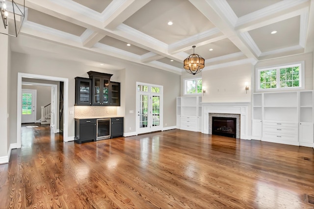 unfurnished living room with an inviting chandelier, wine cooler, wood finished floors, and a fireplace