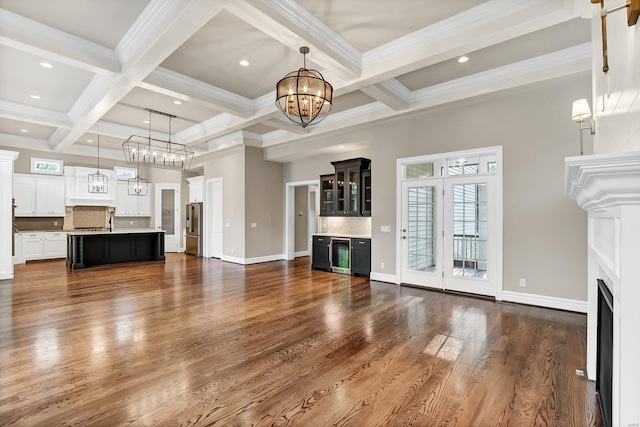 unfurnished living room featuring beam ceiling, coffered ceiling, dark wood-style floors, a fireplace, and a chandelier