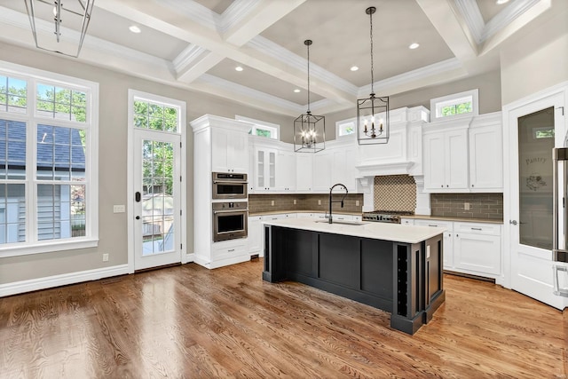 kitchen with a sink, beamed ceiling, double oven, and light wood-style flooring