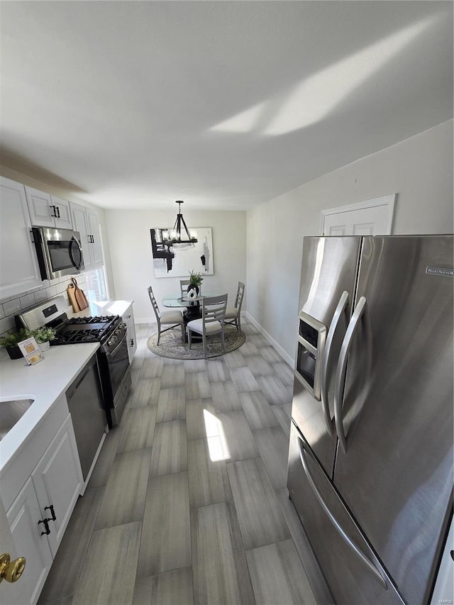 kitchen with appliances with stainless steel finishes, hanging light fixtures, tasteful backsplash, white cabinets, and a chandelier