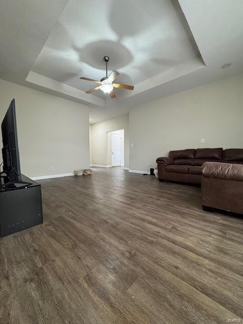 living room featuring ceiling fan, dark wood-type flooring, and a tray ceiling