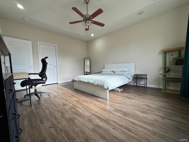 bedroom with ceiling fan, dark wood-type flooring, and a tray ceiling