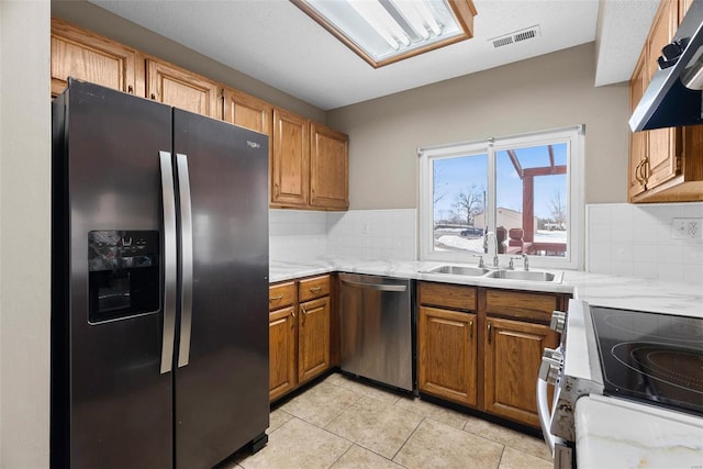 kitchen with sink, light stone counters, light tile patterned floors, stainless steel appliances, and decorative backsplash