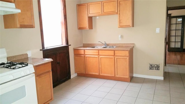 kitchen with light tile patterned flooring, sink, and white gas stove