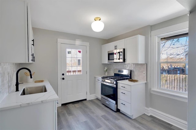 kitchen with white cabinetry, sink, backsplash, light stone counters, and stainless steel appliances