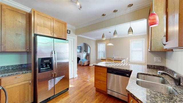 kitchen featuring sink, crown molding, dark stone countertops, appliances with stainless steel finishes, and pendant lighting