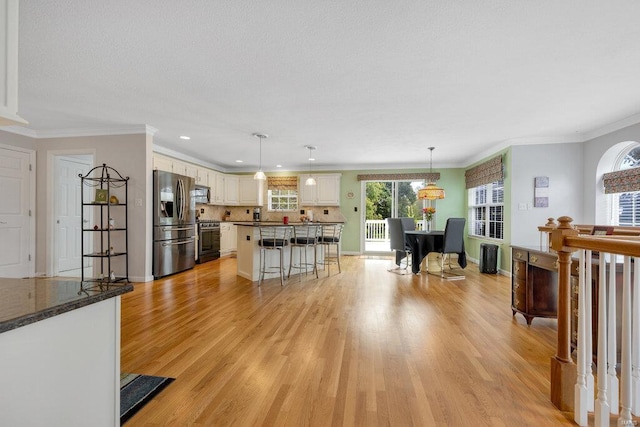 kitchen with decorative light fixtures, a kitchen bar, ornamental molding, light hardwood / wood-style floors, and stainless steel appliances