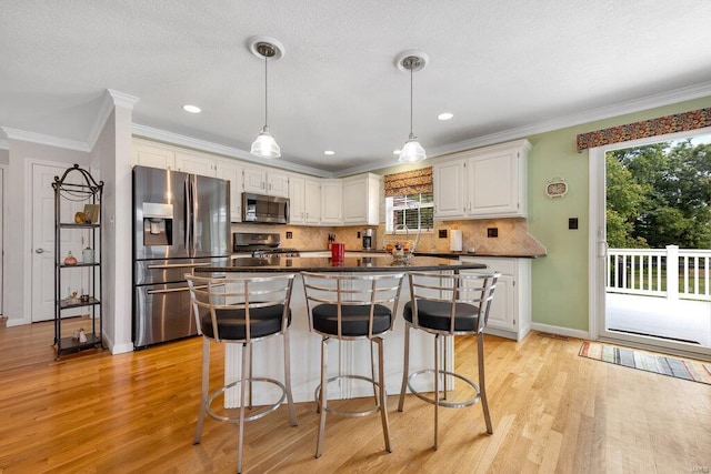 kitchen featuring appliances with stainless steel finishes, white cabinetry, decorative backsplash, ornamental molding, and light wood-type flooring